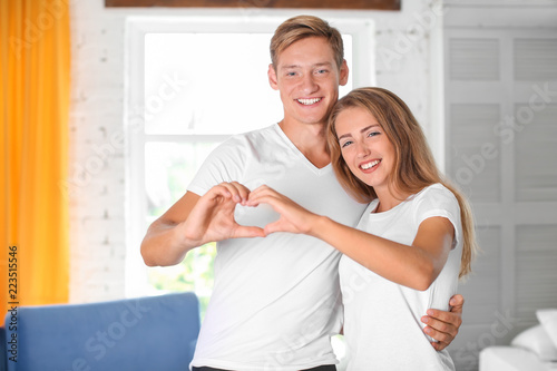 Young couple holding hands in shape of heart at home