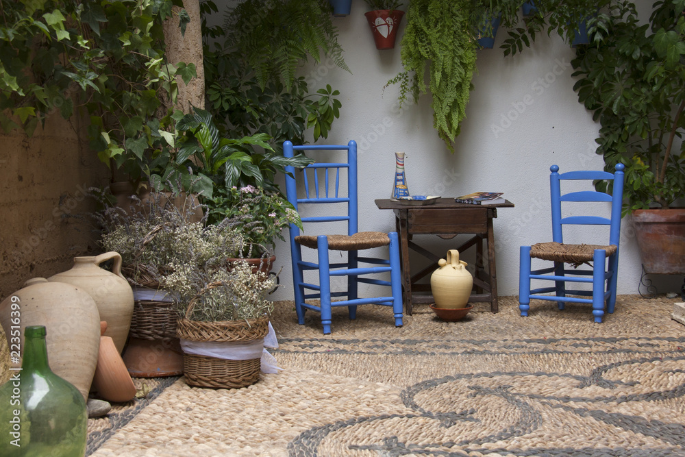 Precioso patio andaluz con plantas, sillas de color azul, mesa de madera y  vasijas colocadas en suelo de piedra con mosaico. Córdoba, Andalucía,  España. Viajes y turismo. foto de Stock | Adobe