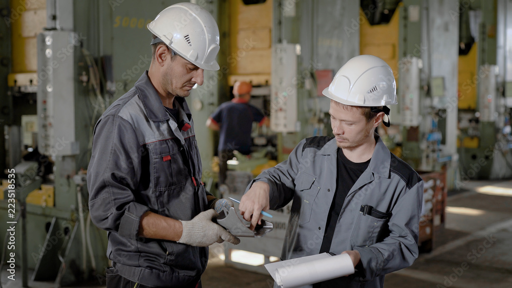two engineers are inspecting sample of metal detail in a workshop, one man is touching surface two engineers are inspecting sample of metal detail in a workshop, one man is touching surface