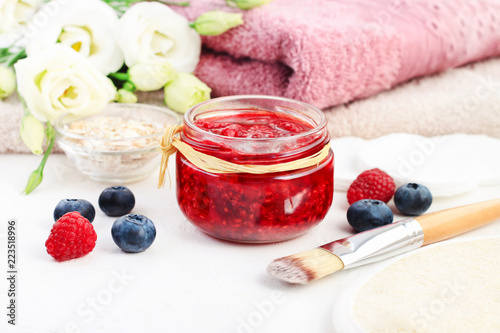 Jar of fruit beauty care mask of mashed red raspberies, flowers and towels spa background, fresh berries for skin exfoliation. 
 photo