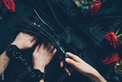 cropped shot of man holding black whip and woman in leather handcuffs photo