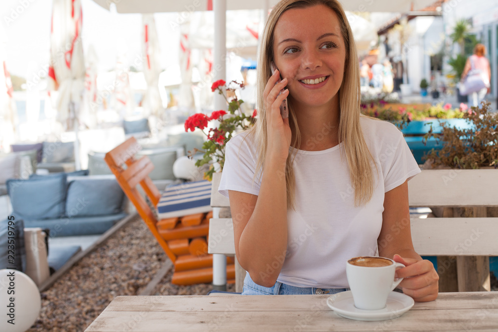 Beautiful smiling young woman talking on the phone and drinking coffee Beautiful smiling young woman talking on the phone and drinking coffee