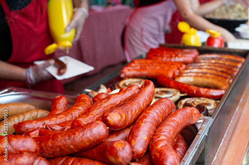 Uncooked european sausages. Grilled sausages and people serving in the background.