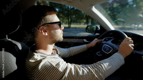 A man is driving a modern car. A handsome man with a beard in the sun protective glasses, confidently steers. © kustvideo
