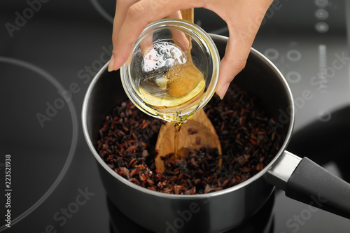 Woman pouring oil into saucepan with boiled rice on stove, closeup