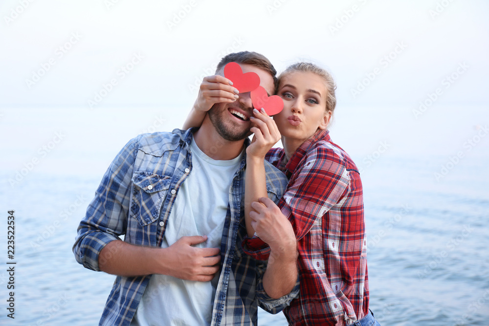Funny young couple with red hearts on sea shore