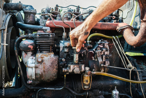 The man repairs the engine in an old tractor on a potato field.