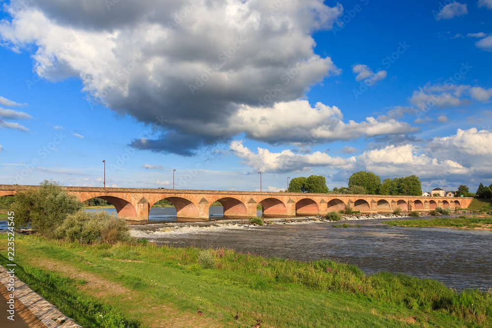 Beautiful summer view of the arched bridge over the river Loire (Pont de Loire) in Nevers, France, with a blue sky with clouds Beautiful summer view of the arched bridge over the river Loire (Pont de Loire) in Nevers, France, with a blue sky with clouds