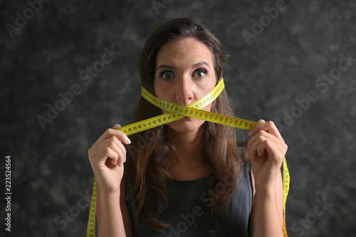 Woman with measuring tape around her mouth on dark background. Diet concept