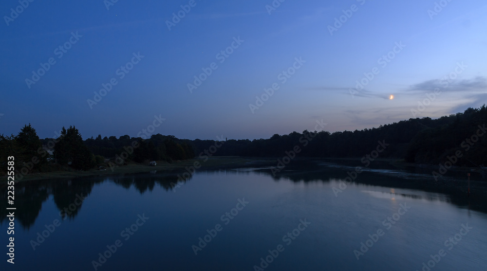 Beautiful dark blue nightscape landscape of the coastal river L'Arguenon after sunset with a new moon rising and reflection in the water near Saint-Malo in Brittany, France
