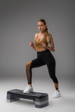 sportive young woman working out on step aerobics board on grey