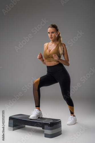 sportive young woman working out on step aerobics board on grey