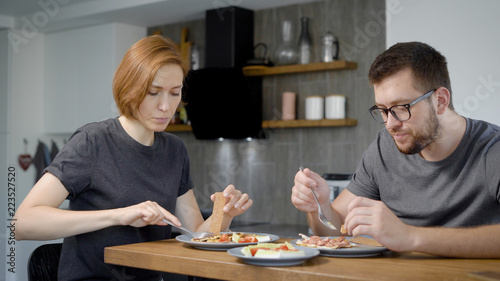 Husband and wife eat breakfast together. Behind the wooden bar, behind the modern kitchen interior.