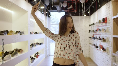 Portrait of young girl laughing using smartphone taking selfie in shopping mall. There are lights decoration on background.
