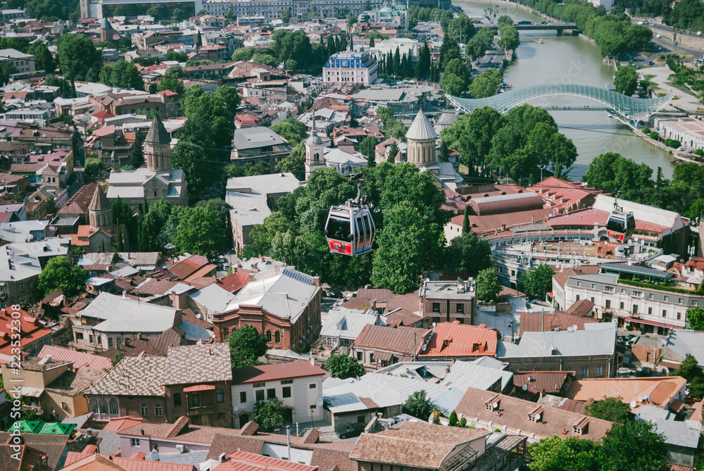 Panoramic view of Old Tbilisi, the capital of Georgia. Cable car over the city. Hot sunny afternoon. Red rooftops of old houses.