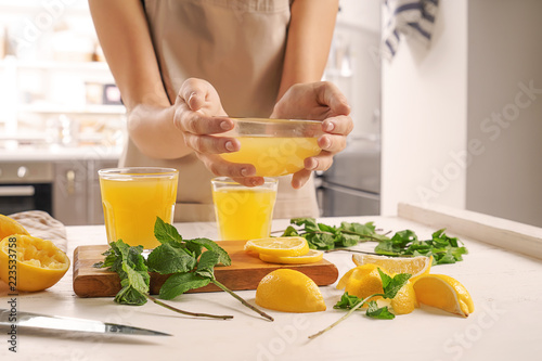 Woman holding glass bowl of fresh lemon juice over table
