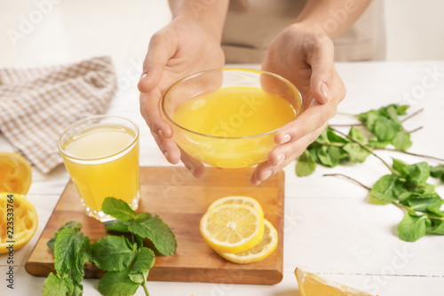Woman holding glass bowl of fresh lemon juice over table