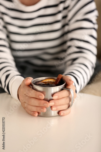 Woman holding cup of delicious mulled wine at table, closeup