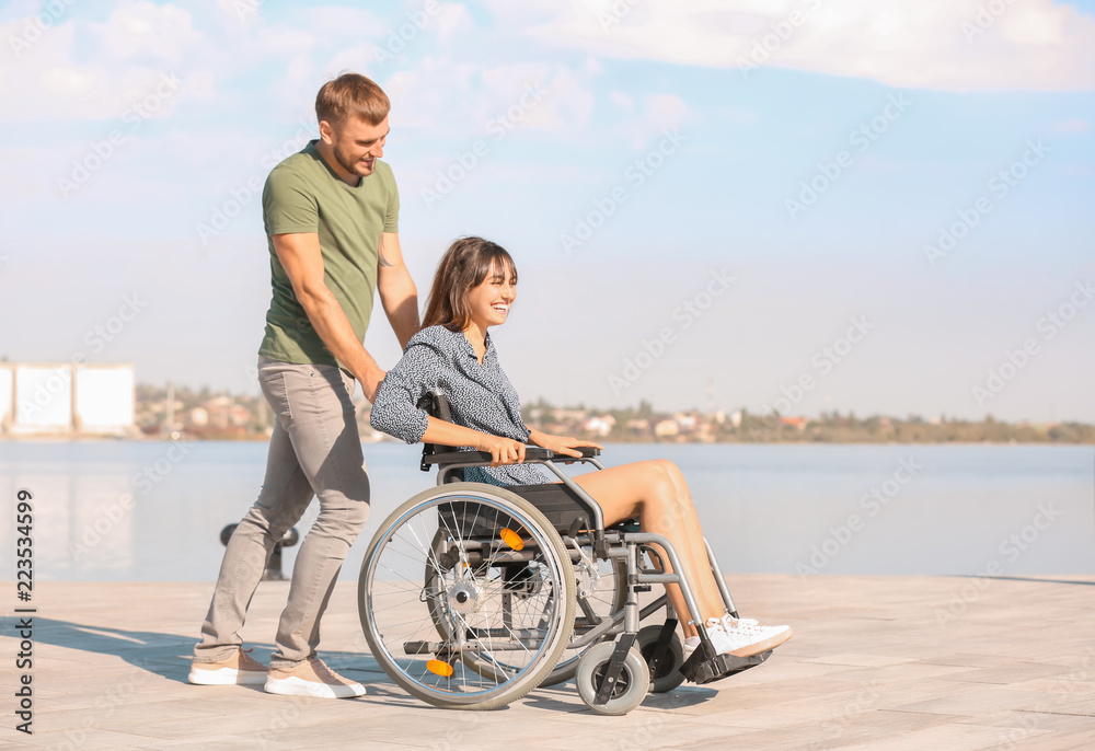 happy young woman in wheelchair and her husband near river happy young woman in wheelchair and her husband near river