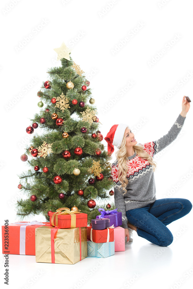 happy woman sitting near christmas tree with gifts and taking selfie on smartphone, isolated on white happy woman sitting near christmas tree with gifts and taking selfie on smartphone, isolated on white