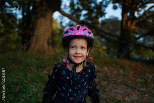 Portrait of a laughing little girl in a helmet and elbow pads. Little roller skater is in outdoor activity in autumn park. Concept - healthy lifestyle.