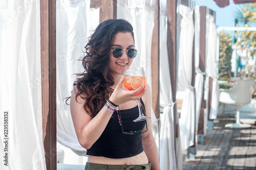Young brunette woman driking alcoholic red orange cocktail with orange and vintage sunglasses in a terrace Ibiza