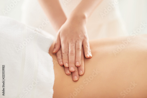 Crop hands of female therapist rubbing loin of female client during massage session in spa salon photo