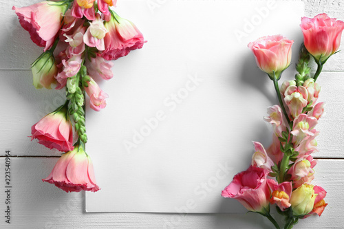 Beautiful blooming flowers and empty sheet of paper on white wooden table