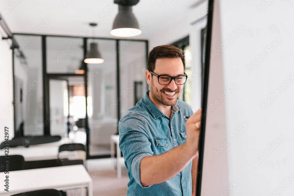 Fototapeta premium Smiling young man writing on a flipchart.