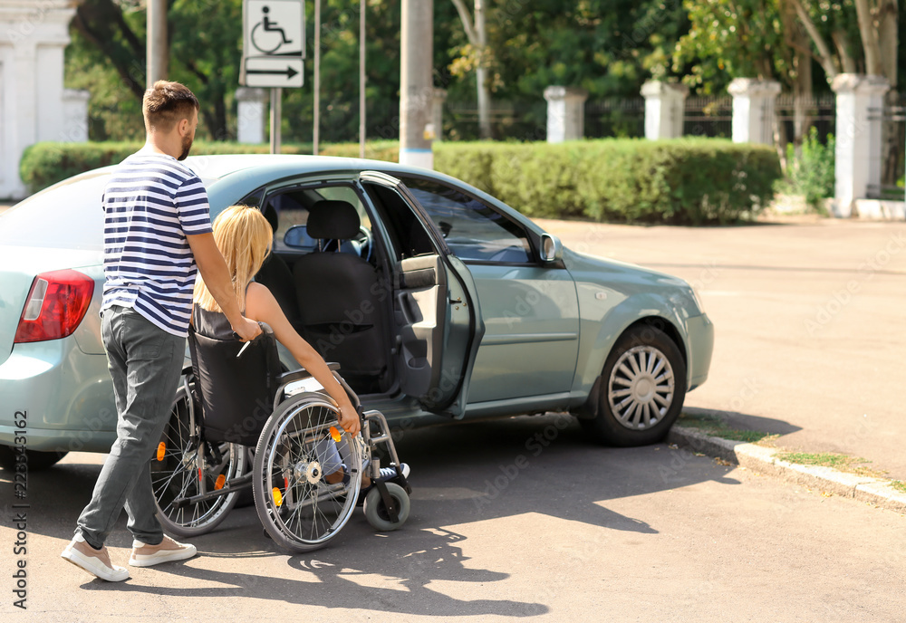 Naklejka premium Man helping woman in wheelchair to sit in car