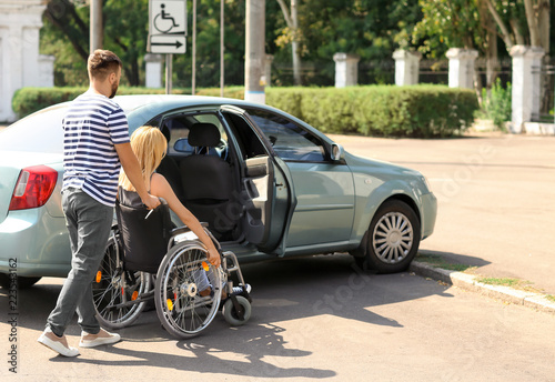 Man helping woman in wheelchair to sit in car © Pixel-Shot