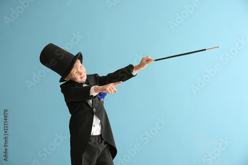 Cute little magician showing trick on color background