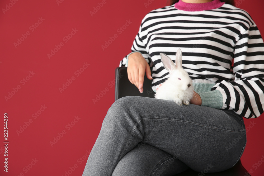 Beautiful young woman with cute bunny sitting on chair against color background Beautiful young woman with cute bunny sitting on chair against color background