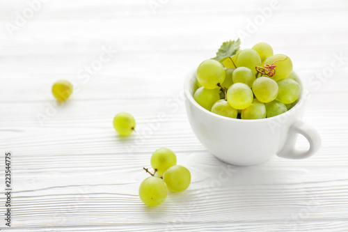 Cup with sweet grapes on white wooden table