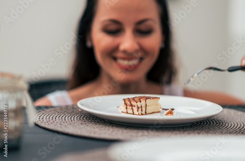 Young woman at the table ooking at cake. Focus on cake. photo