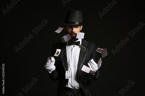 Magician showing tricks with cards on dark background