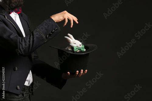 Magician holding hat with rabbit on dark background