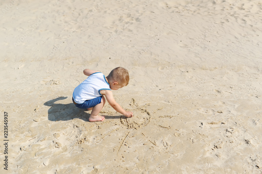 Baby boy draws a sun in the sand on the beach. Baby boy draws a sun in the sand on the beach.