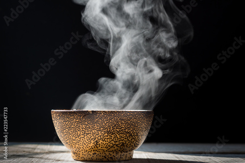 Steam of hot soup with smoke in a soup black ceramic bowl on dark background.selective focus