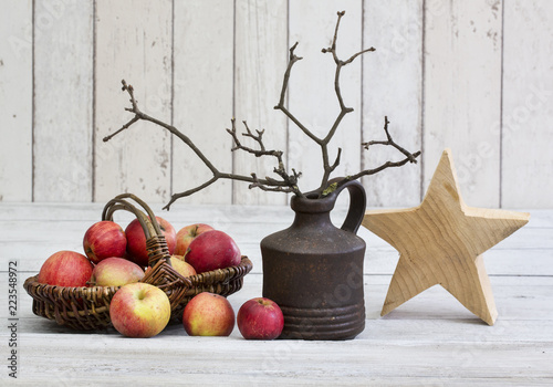 Rustic decoraton with apples, wooden star and twigs in a vase on a white wooden background, perfect for scandi-chic style winter and autumn mood photo