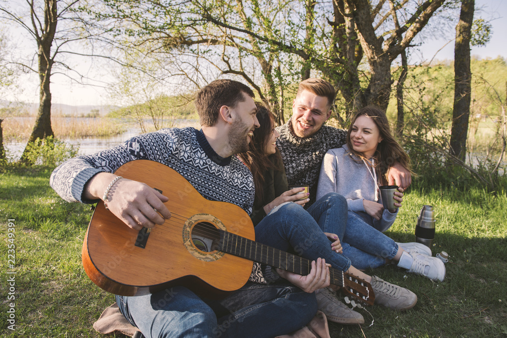 Two friendly young couple resting together outside. Autumn vacation. Man playing guitar Two friendly young couple resting together outside. Autumn vacation. Man playing guitar