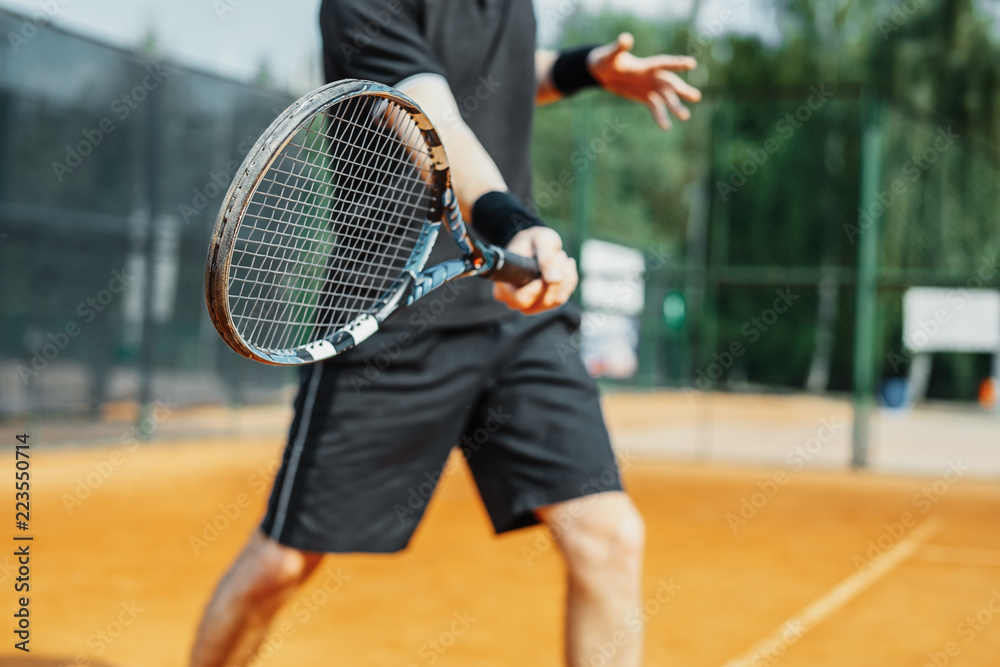 Close up of man playing tennis at court and beating the ball with a racket.