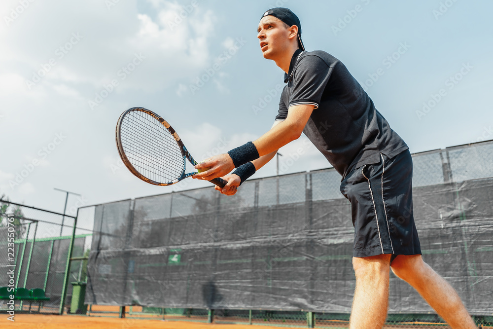Young man playing tennis at tennis and serving a ball with straighten strike.