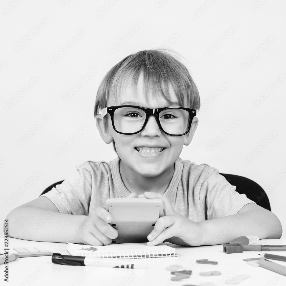 Happy smart boy in big glasses, sits at desk, looking to camera