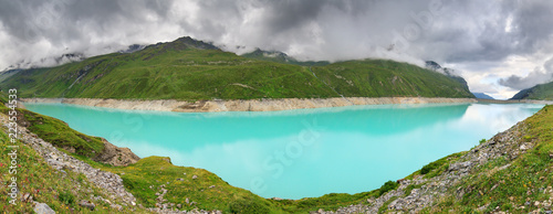 Beautiful 180 degree panoramic view of reservoir lake Moiry (lac de Moiry) with vibrant turquoise blue water at a low level in summer in Valais, Switzerland