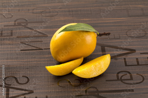 A Mango with leaf and stem and some cut slices of mango on brown background