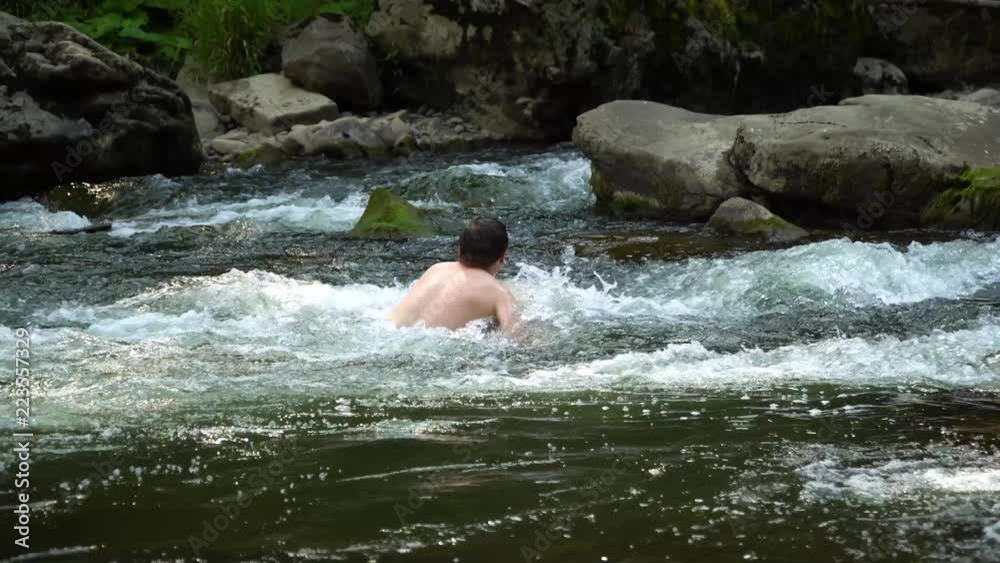 The guy is swimming in the river. A young cute guy bathes in a clean mountain river. He is happy. The guy is swimming in the river. A young cute guy bathes in a clean mountain river. He is happy.