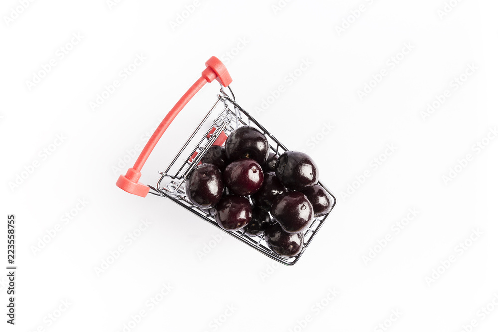 group of fresh red cherries in a small shopping cart on a white background
