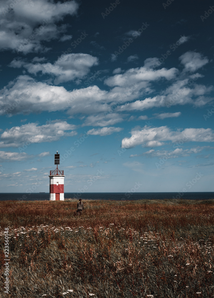 A girl and a lonely red-white lighthouse in an autumn field on the shores of the Okhotsk Sea in the north of the Khabarovsk Territory of Russia