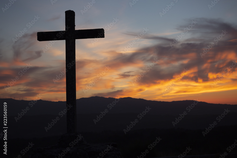 Religion theme, view of catholic cross in black shadow, with fantastic sunset with warm colors and mountains as background, in Viseu, Portugal